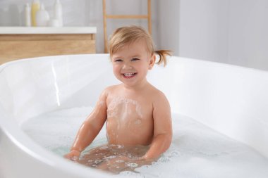 Şirin küçük kız evde köpüklü banyo yapıyor.