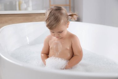Şirin küçük kız evde köpüklü banyo yapıyor.
