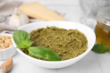 Lezzetli pesto soslu kase ve beyaz masada taze fesleğen, yakın plan.