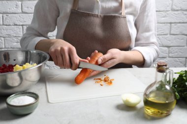Beyaz masada haşlanmış havuç soyan kadın, yakın plan. Sirkeli salata pişiriyorum.