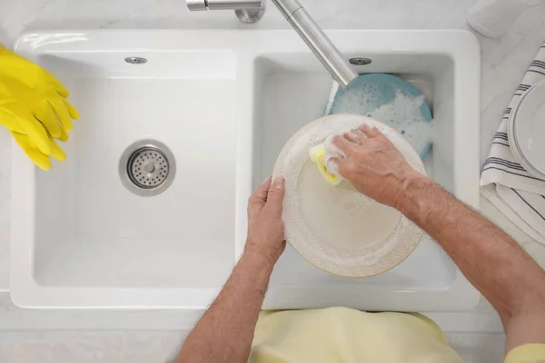 Man washing plate above sink, top view