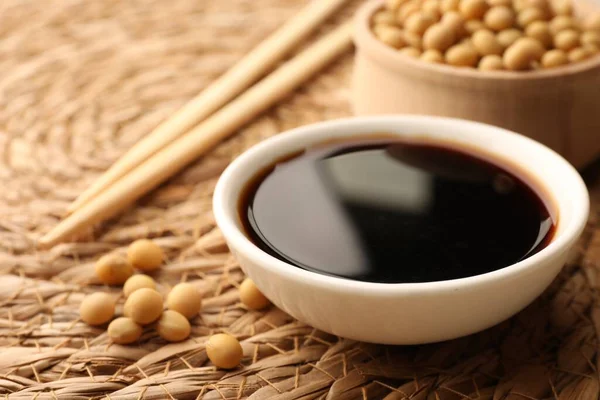 stock image Soy sauce in bowl and soybeans on wicker mat, closeup