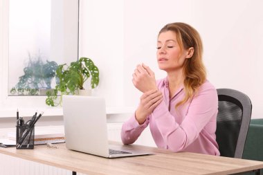 İçerideki ahşap masada dizüstü bilgisayar kullanırken bileği ağrıyan bir kadın. Artrit belirtileri