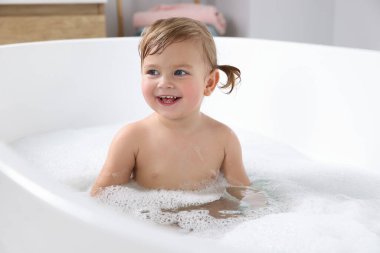 Şirin küçük kız evde köpüklü banyo yapıyor.