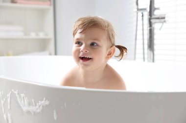 Şirin küçük kız evde köpüklü banyo yapıyor.
