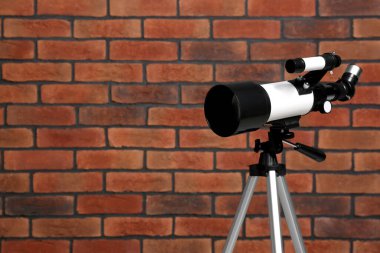 Tripod with modern telescope near brick wall. Space for text