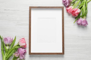 Boş fotoğraf çerçevesi ve beyaz ahşap masa üzerinde güzel çiçekler. Tasarım için boşluk