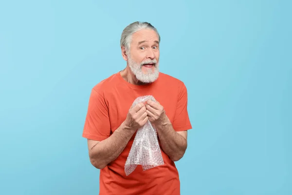 Emotional Senior Man Popping Bubble Wrap Light Blue Background Stress — Stock Photo, Image