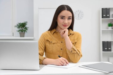 Ofiste dizüstü bilgisayarla çalışan genç bir kadın stajyer.