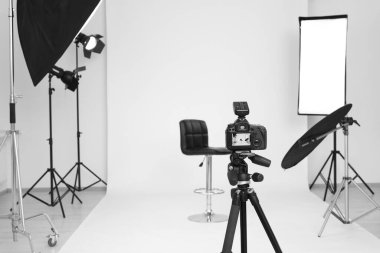 Camera on tripod, bar stool and professional lighting equipment in modern photo studio