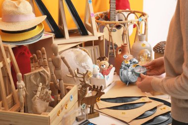 Masanın yanında bir sürü farklı eşyası olan alarmlı saati tutan kadın, yakın plan. Garaj satışı