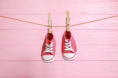 Şirin bebek ayakkabıları, pembe ahşap duvarda çamaşır ipinde kurulanıyor.
