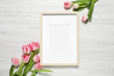 Boş fotoğraf çerçevesi ve beyaz ahşap masa üzerinde güzel çiçekler. Tasarım için boşluk
