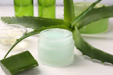 Kozmetik jel kavanozu ve aloe vera yaprakları beyaz ahşap masada, yakın plan.
