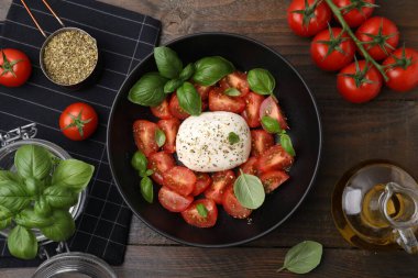 Mozarella, domates, fesleğen ve diğer malzemelerle ahşap masa üzerinde lezzetli bir Caprese salatası.