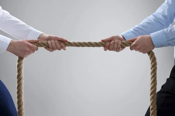 Dispute concept. Men pulling rope on light grey background, closeup. Space for text