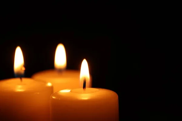 stock image Burning wax candles on black background, closeup. Space for text