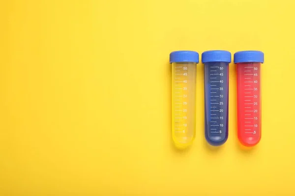 Test tubes with colorful liquids on yellow background, flat lay and space for text. Kids chemical experiment set
