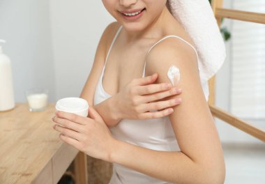 Genç bir kadın omuz kremi sürüyor, kapalı alanda, yakın plan.