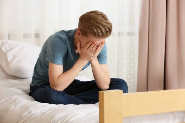 Mutsuz genç çocuk evde elleri yatakta yüzünü örtüyor.