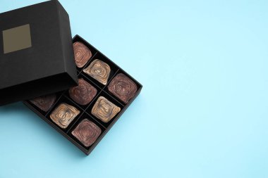 Box of tasty chocolate candies on light blue background, top view. Space for text