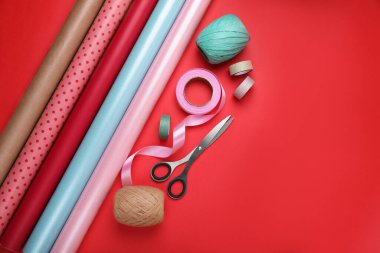 Kırmızı arka planda ambalaj kağıtları, makas ve kurdeleler, düz yatış. Metin için boşluk