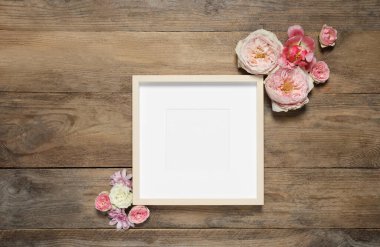 Boş fotoğraf çerçevesi ve ahşap masanın üzerinde güzel çiçekler, düz bir şekilde yatıyordu. Tasarım için boşluk