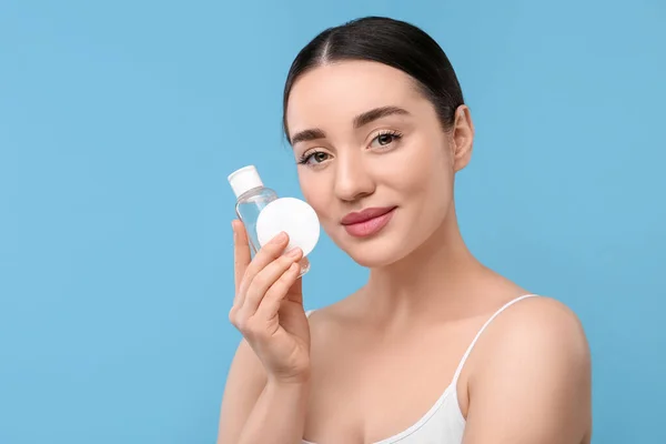 Stock image Beautiful woman with makeup remover and cotton pad on light blue background, space for text