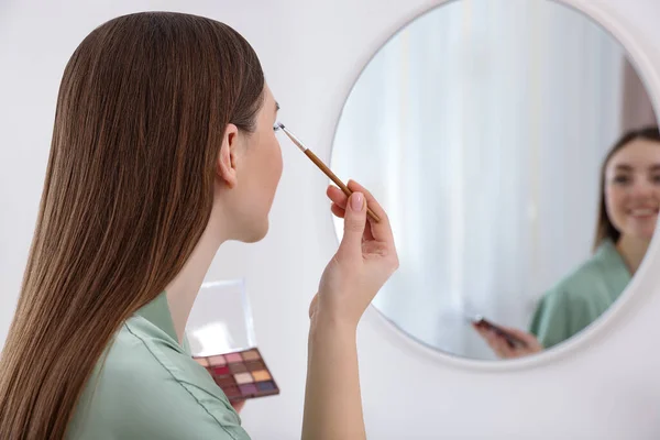 Vacker Ung Kvinna Som Applicerar Ögonskugga Med Borste Nära Spegeln — Stockfoto
