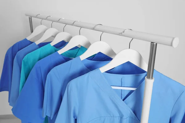 Different medical uniforms on rack against light grey background
