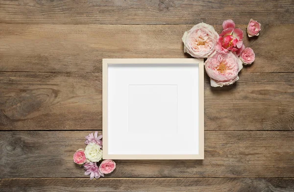 stock image Empty photo frame and beautiful flowers on wooden table, flat lay. Space for design