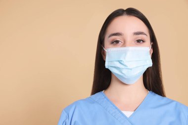 Açık kahverengi arka planda koruyucu maske takan hemşire, mesaj için boşluk