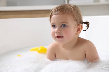 Şirin küçük kız evde köpüklü banyo yapıyor.