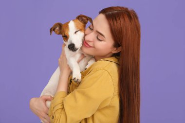 Kadın menekşe arka planda sevimli Jack Russell Terrier köpeğine sarılıyor.