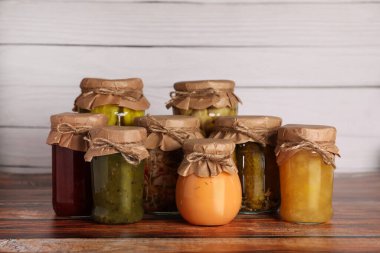 Ahşap masada farklı malzemelerle korunmuş bir sürü kavanoz.