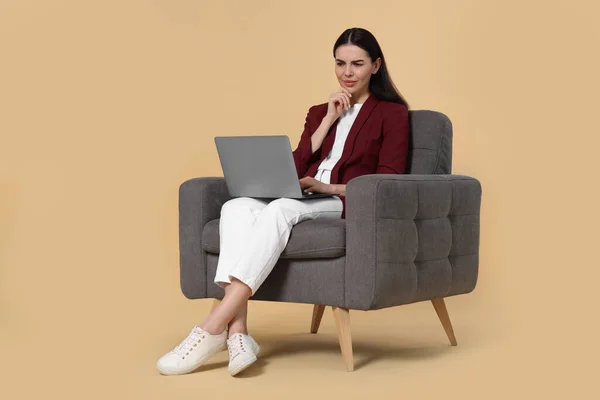 Verward Vrouw Met Laptop Zittend Fauteuil Beige Achtergrond — Stockfoto