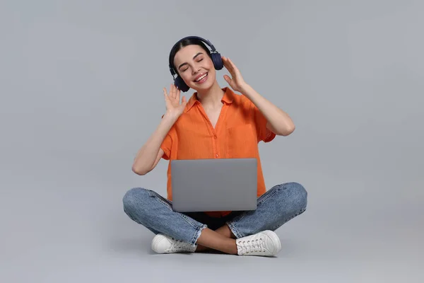 Ευτυχισμένη Γυναίκα Φορητό Υπολογιστή Ακούγοντας Μουσική Ακουστικά Ανοιχτό Γκρι Φόντο — Φωτογραφία Αρχείου