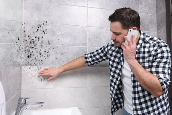 霉菌清除服务 男人在电话里说话 看着浴室里受影响的墙壁 — 图库照片
