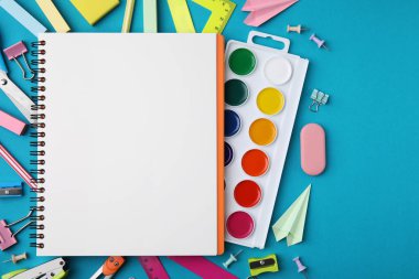 Açık mavi arkaplanda farklı okul kırtasiyesi ve defter, metin için boş alan. Okula geri dön.