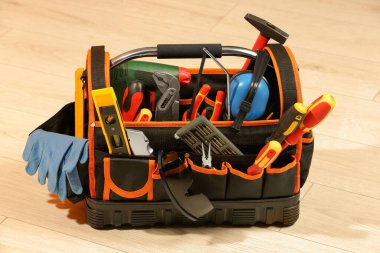 Beyaz ahşap masada tamir için farklı aletler içeren çanta.