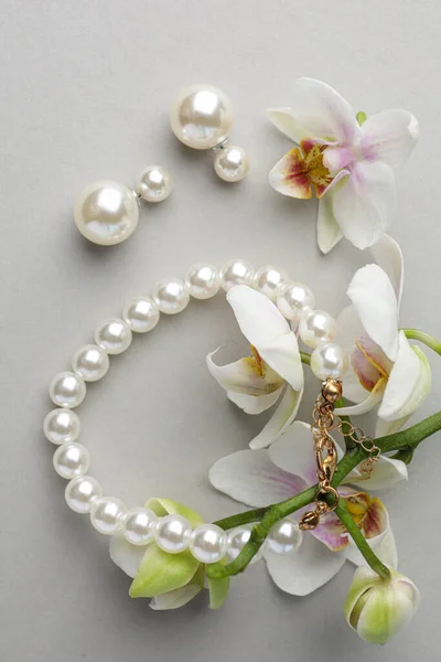 白色背景的精致珍珠耳环 手镯和兰花 — 图库照片