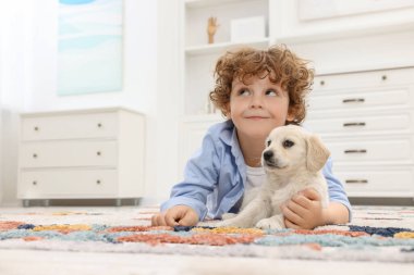 Evdeki halıda sevimli bir köpek yavrusuyla yatan küçük çocuk. Metin için boşluk