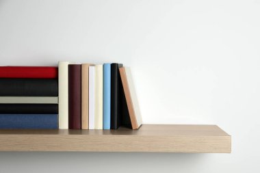 Beyaz duvarın yanındaki ahşap rafta bir sürü ciltli kitap var. Metin için boşluk