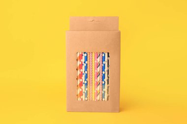 Box with many paper drinking straws on orange background