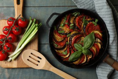 Lezzetli ratatouille ve açık mavi ahşap masa üzerindeki malzemeler.