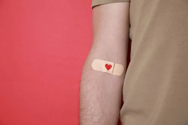 Blood donation concept. Man with adhesive plaster on arm against red background, closeup. Space for text