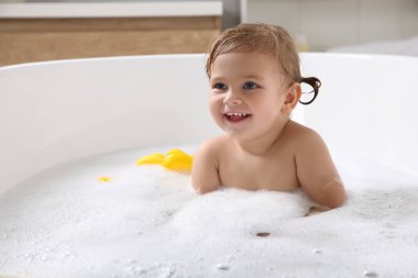 Şirin küçük kız evde köpüklü banyo yapıyor.
