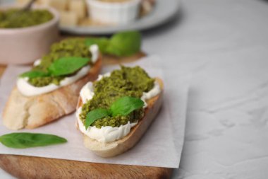 Krem peynirli lezzetli bruschettalar, pesto sosu ve beyaz masada taze fesleğen, yakın plan. Metin için boşluk