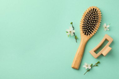 Tahta saç fırçası, çiçek dalları ve turkuaz arka planda toka, düz yatış. Metin için boşluk