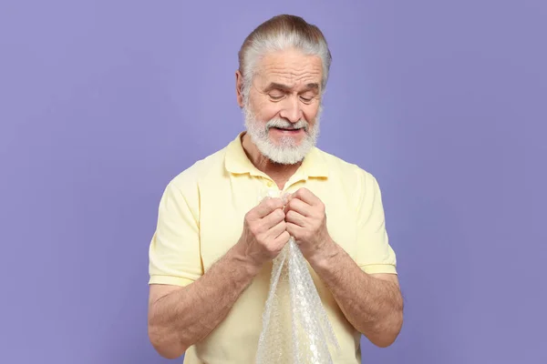 Senior Man Popping Bubble Wrap Light Purple Background Stress Relief — Stock Photo, Image